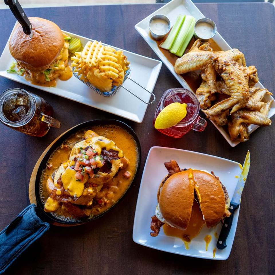 Table laden with burgers, waffle fries, chicken wings, and drinks, viewed from above.