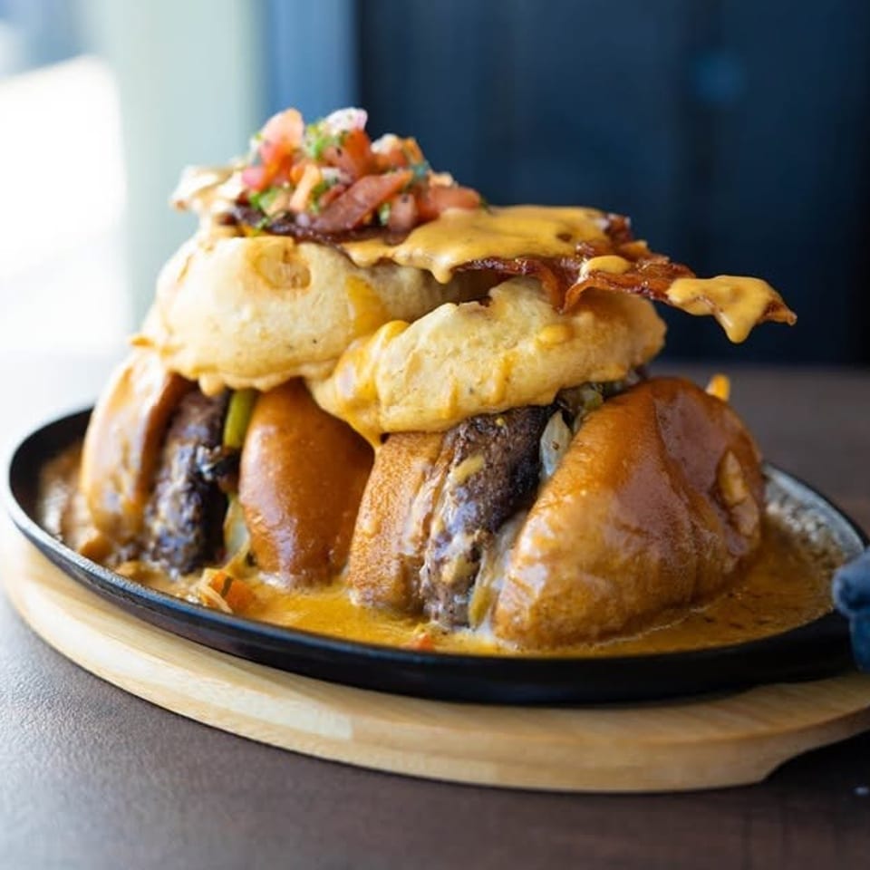 Stacked cheesy burgers with bacon and vegetable toppings served in a skillet with creamy sauce.